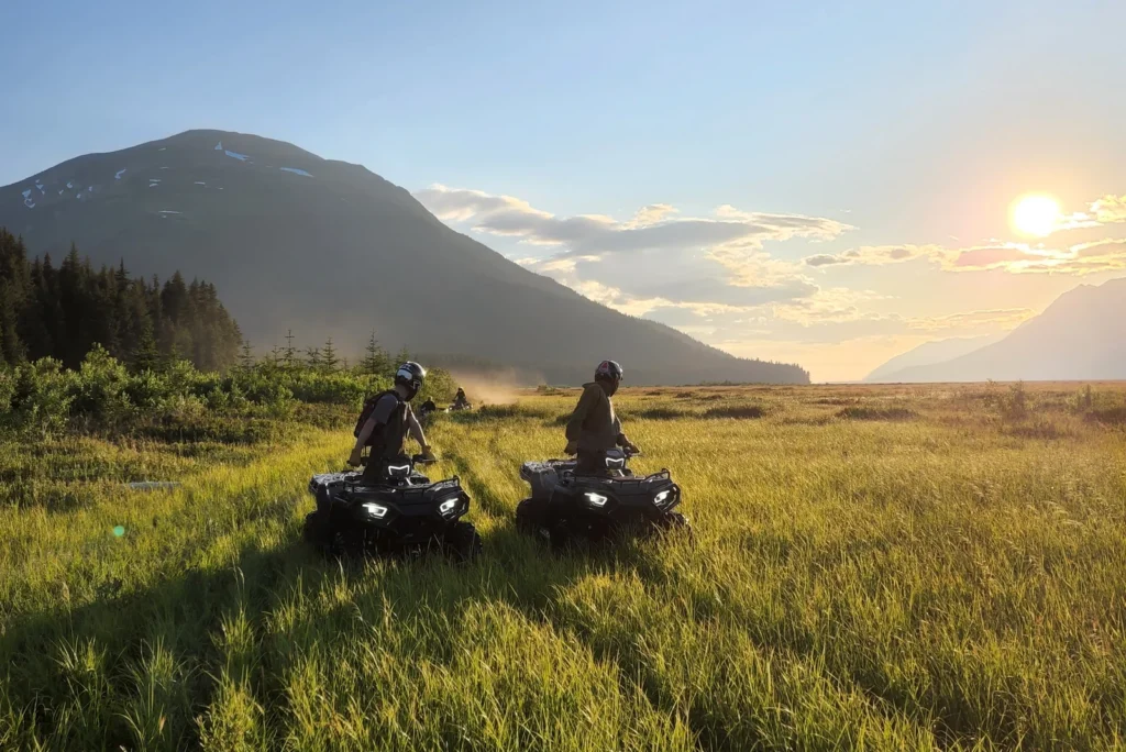 ATV riders in a green meadow beneath evening mountain light